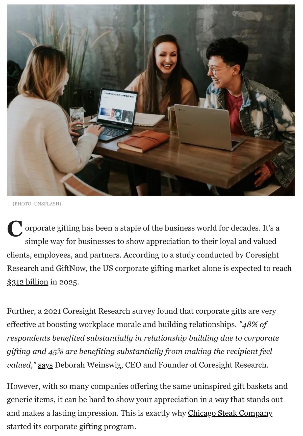 Three people sitting at a table with laptops, engaged in a discussion.