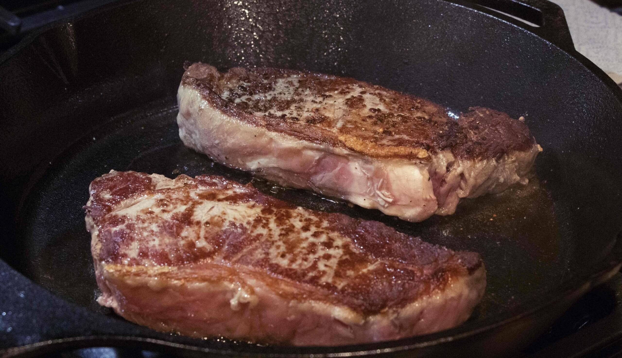 pan frying steaks on iron skillet