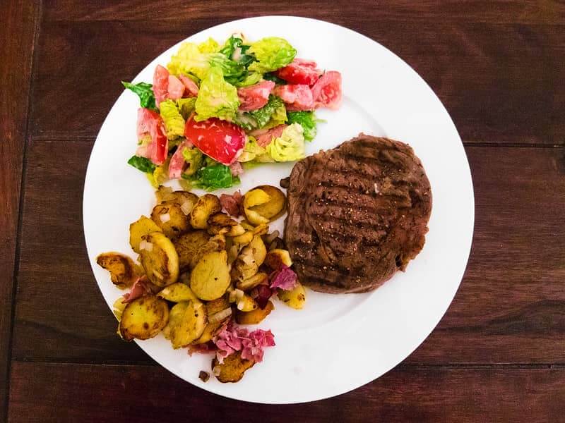 ribeye steak with sides - fried potatoes and salad 