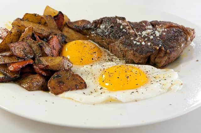 t-bone steak and eggs with potatoes on a platter