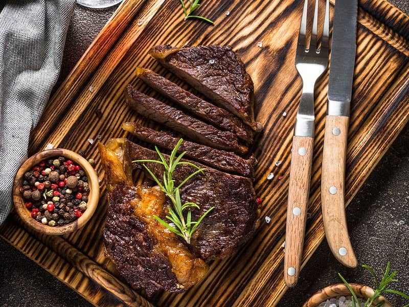 Pan seared ribeye steak on cutting board with steak fork and knife